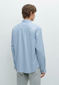 Himmelblaues Langarmhemd mit geknöpften Manschetten, geradem Saum und weicher Stoffstruktur. Die Rückansicht zeigt einen klassischen Kragen und ein minimales Design.