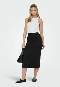 Schwarzer, figurbetonter Midirock mit hoher Taille und seitlichen Nähten, kombiniert mit einem weißen ärmellosen Oberteil und schwarzen flachen Schuhen. Schwarze Handtasche inklusive.