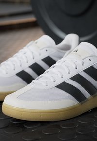 White sports shoes with black stripes, made of mesh and leather, featuring a textured surface and a gum rubber outsole.