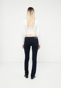 Jeans ajustados azules de denim, con una cintura de media altura y bolsillos traseros. Combinados con un top corto blanco, el modelo se ve desde atrás.