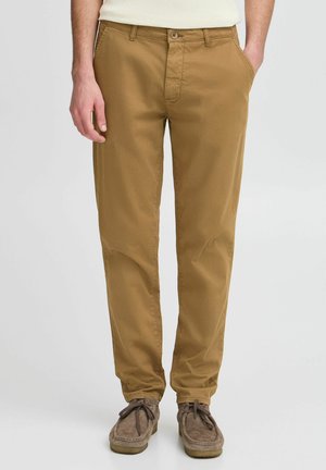 Pantalones de algodón marrón de corte recto, con cierre de cremallera, bolsillos frontales y un único bolsillo trasero, combinados con zapatos de ante marrones.