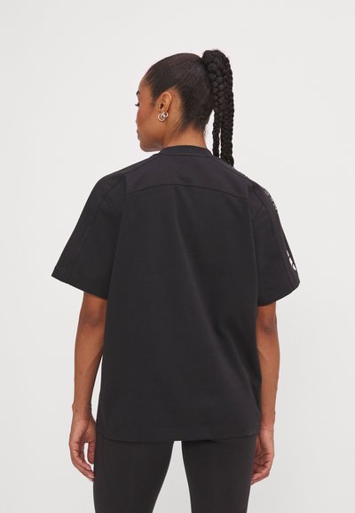 Chemise noire à manches courtes avec une coupe décontractée, texture unie et détails subtils aux épaules. Portée avec des leggings noirs assortis.