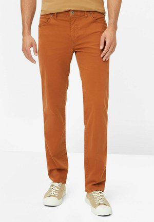 Braune Baumwollhosen mit geradem Bein-Design, Fünf-Taschen-Styling und einem kontrastierenden Knopfverschluss. Kombiniert mit beigen Sneakers.