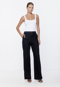 Czarne dżinsy o szerokich nogawkach i wysokim stanie, z kieszenią z przodu i zapięciem na guzik. Połączone z dopasowanym białym topem na ramiączkach.