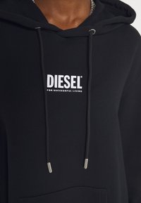 Schwarzer Hoodie aus weichem Stoff, mit einer Fronttasche, Kordeln mit metallischen Enden und einem weißen "DIESEL"-Logo, das zentral auf der Brust platziert ist.