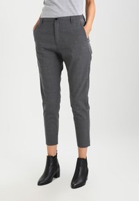 Grå skräddarsydda byxor med en texturerad yta, utrustade med två sidfickor och en avsmalnande bendesign. Bärs med svarta ankelstövlar.