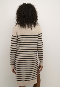 Robe pull en beige avec des rayures horizontales noires, dotée de manches longues, d'une texture côtelée et de fentes sur les côtés pour un confort de mouvement.
