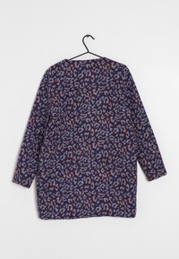 Cardigan lavorato a maniche lunghe con motivo astratto in blu, bordeaux e rosa chiaro, appeso a un gancio nero su uno sfondo bianco.