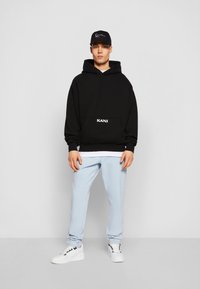 Black oversized hoodie with a front pocket and "KANI" text. Light blue joggers with elastic cuffs. White sneakers complete the outfit.