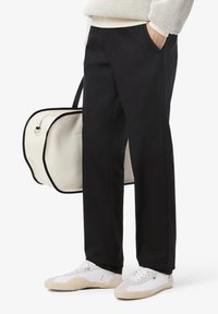 Pantaloni neri in cotone con tasche laterali, abbinati a sneakers bianche. Una borsa crema con bordi neri è appesa sulla spalla.