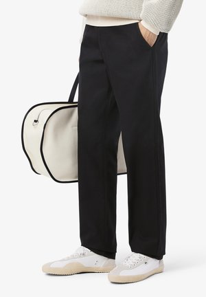 Pantalons noirs en coton avec poches latérales, associés à des baskets blanches. Un sac crème avec des finitions noires est porté sur l'épaule.
