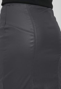 Jupe en cuir gris taille haute avec une texture lisse, présentant des coutures courbes et des détails subtils sur le côté pour un ajustement sur mesure.