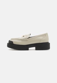 Beige lakschoen loafers met een ronde neus, gouden hardwareaccent en een chunky zwart rubberen platformzool met verticale groeven.