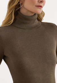 Sweater de gola alta castanho, feito em tecido de malha suave, com um design justo e colarinho canelado, apresentando uma textura lisa e sem padrões visíveis.