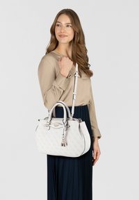 Sac à main blanc avec motif de logo en relief, forme structurée, doubles poignées et une bandoulière amovible. Détails en métal et pampille.