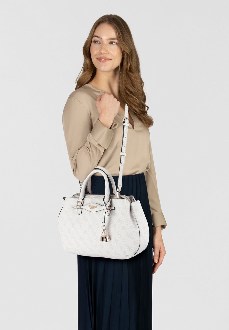 Sac à main blanc avec motif de logo en relief, forme structurée, doubles poignées et une bandoulière amovible. Détails en métal et pampille.
