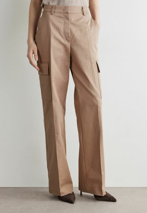 Pantalon cargo beige à jambes larges avec poches à rabat, porté avec des escarpins marron à bout pointu et un haut beige rentré.