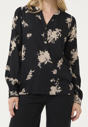 Sort bluse med lange ærmer med beige blomsterprint, V-hals med fire knapper, båret med sorte bukser.
