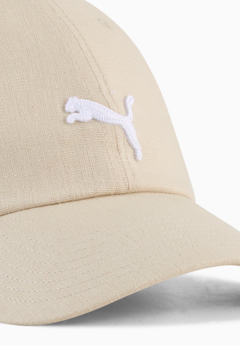 Casquette beige avec une visière incurvée, fabriquée en tissu texturé. Présente un logo Puma brodé blanc à l'avant.