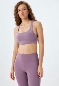 Lila atletisk crop top med breda axelband, slät textur och en figursydd design, ihop med matchande högmidjade leggings.