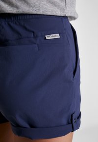 Pantalones cortos azul marino hechos de un material ligero, con dobladillo acampanado, bolsillos laterales y una etiqueta con el logo de Columbia en la parte posterior.