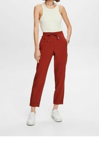 Czerwone, zwężane spodnie z elastycznym pasem, posiadające boczne kieszenie i ściągnięte u dołu. W zestawie z kremowym topem na ramiączkach i białymi trampkami.
