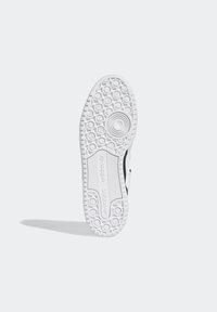 Suola di sneaker, prevalentemente in gomma bianca con motivi circolari testurizzati e branding. Presenta una leggera curva e un'area centrale di presa rialzata.