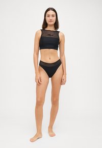 Melns divdaļīgs peldkostīms, kas ietver topu ar acs detaļām un atbilstošu bikini apakšdaļu ar acs akcentiem viduklī.
