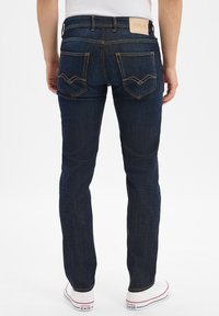 Mörkblå denimjeans med en åtsittande design, som har kontrasterande orange sömmar, två bakfickor och en strukturerad läderlogotyp.