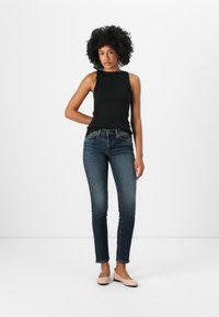 Zwarte geribbelde tanktop en donkere skinny jeans. Model draagt lichtroze flats. Eenvoudig ontwerp, slim fit silhouet, geen zichtbare patronen of accenten.