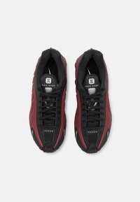 Nike Shox sportbačiai juodos ir bordo spalvų. Yra tekstūruota viršutinė dalis, paminkštintas apykaklė ir plokščios raišteliai. Išskirtinis logotipas ant liežuvio ir kulno.
