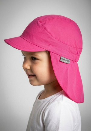 Toddler wearing a bright pink sun hat with neck flap and short brim, smiling, against a plain light background.