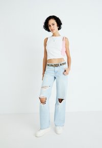 Λευκή κοντή μπλούζα, ανοιχτό μπλε σκισμένα τζιν με φαρδιές γάμπες, ζώνη με σχέδιο λεοπάρ και λευκά αθλητικά παπούτσια. Τα αξεσουάρ περιλαμβάνουν μία ροζ τσάντα ώμου.