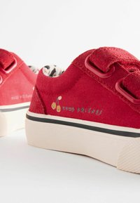 Des baskets en toile rouges avec une texture lisse, des accents circulaires et des motifs de cerises imprimés avec l'étiquette "BONS AMIS". Semelles blanches épaisses.