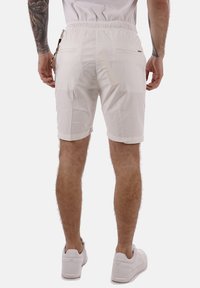 Pantalones cortos de algodón blancos con una cinturilla elástica, dos bolsillos traseros y puños doblados. Llevados con zapatillas blancas. Diseño simple y funcional.