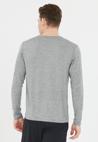 Långärmad grå skjorta med texturerad finish, rund halsringning och åtsittande ärmar, i kombination med svarta sportbyxor.