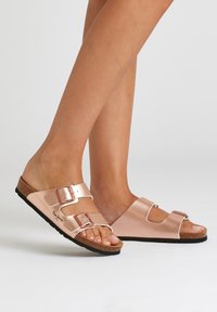 Roze metallic slide sandalen met twee verstelbare gespen, een kurken voetbed en een textuur van zwart rubber aan de onderkant. Minimalistisch ontwerp.