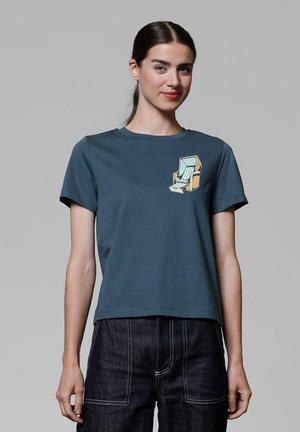 T-shirt à manches courtes en teal fabriqué en coton doux, avec un graphique sur le devant représentant une chaise longue rayée en beige et bleu clair.