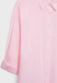 Lyserød langærmet skjorte med knaplukning foran og opfoldet manchet på det ene ærme, isoleret på ensfarvet baggrund.