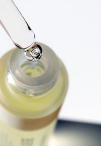 Duidelijke glazen fles met een zilveren pipet; de fles bevat een lichtgele vloeistof. De pipet heeft een afgeronde punt met een druppel die aan het einde vormt.