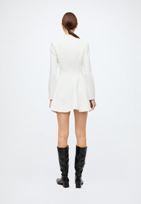White fitted dress with long sleeves, flared skirt, and a high neckline. Worn with knee-high black leather boots. Smooth texture.