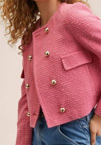 Chaqueta de tweed rosa con un corte cuadrado, que presenta detalles de botones dorados, bolsillos delanteros, tejido texturizado y mangas largas.