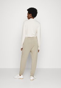 Camisola de manga longa cremosa, calças de jogger bege com cintura elástica, bolsos laterais e punhos ajustados; combinadas com ténis brancos com detalhes em dourado.