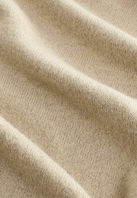 Beige neulekangas, jossa on pehmeä, teksturoitu pinta, sisältäen hienovaraisen kuvion eri sävyissä yhdistelemistä langoista.