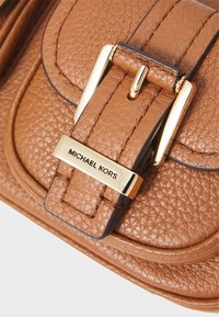 Sac en cuir texturé brun avec un détail de boucle en ton or. Il comprend une étiquette rectangulaire embossée avec "MICHAEL KORS" au niveau du fermoir.