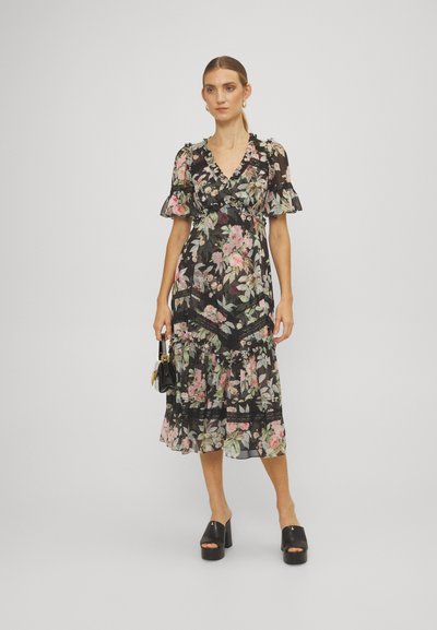 Zwart bloemen midi-jurk met gerimpelde mouwen, gekenmerkt door roze en groene bloemen, gelaagde rok met kantaccenten, gedragen met chunky zwarte sandalen met hak.