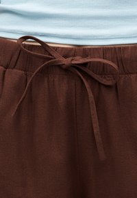 Pantalon marron à cordon noué en nœud à la taille, porté avec un haut côtelé bleu clair.