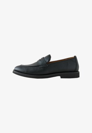 Mocassin homme en cuir noir à surface texturée, style slip-on, petit talon et détail d'une bride sur le dessus.