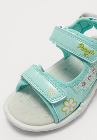 Aqua-Sandale mit zwei Klettverschlüssen, floralen Mustern, pinken Akzenten und einer strukturierten Innensohle. Der Zehenbereich ist offen und hat eine abgerundete Form.