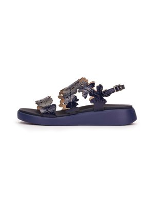 Sandalia de plataforma negra con tiras texturizadas en forma de hoja y hebilla ajustable en el tobillo, suela plana acolchada para mayor comodidad.